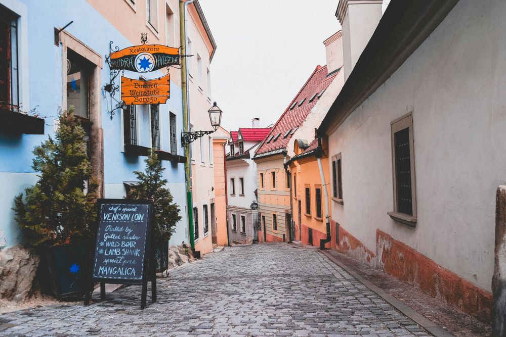 Kopfsteingepflasterte Gasse in der Bratislavaer Altstadt mit schmiedeeisernem Wirtshausschild und einer handgeschriebenen Tageskarte auf einer Tafel