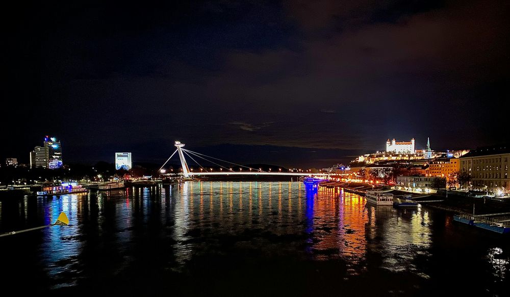 Nächtliches Donaupanorama von Bratislava mit beleuchteter Brücke, Burg auf dem Hügel und Lichtspiegelungen im Wasser